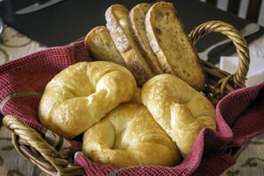 A basket containing several types of bread, including croissants and baguettes, placed on a table with a patterned tablecloth.