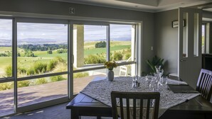A dining area with a table set for six, large windows offering a view of a green landscape, and a door leading to an outdoor deck.