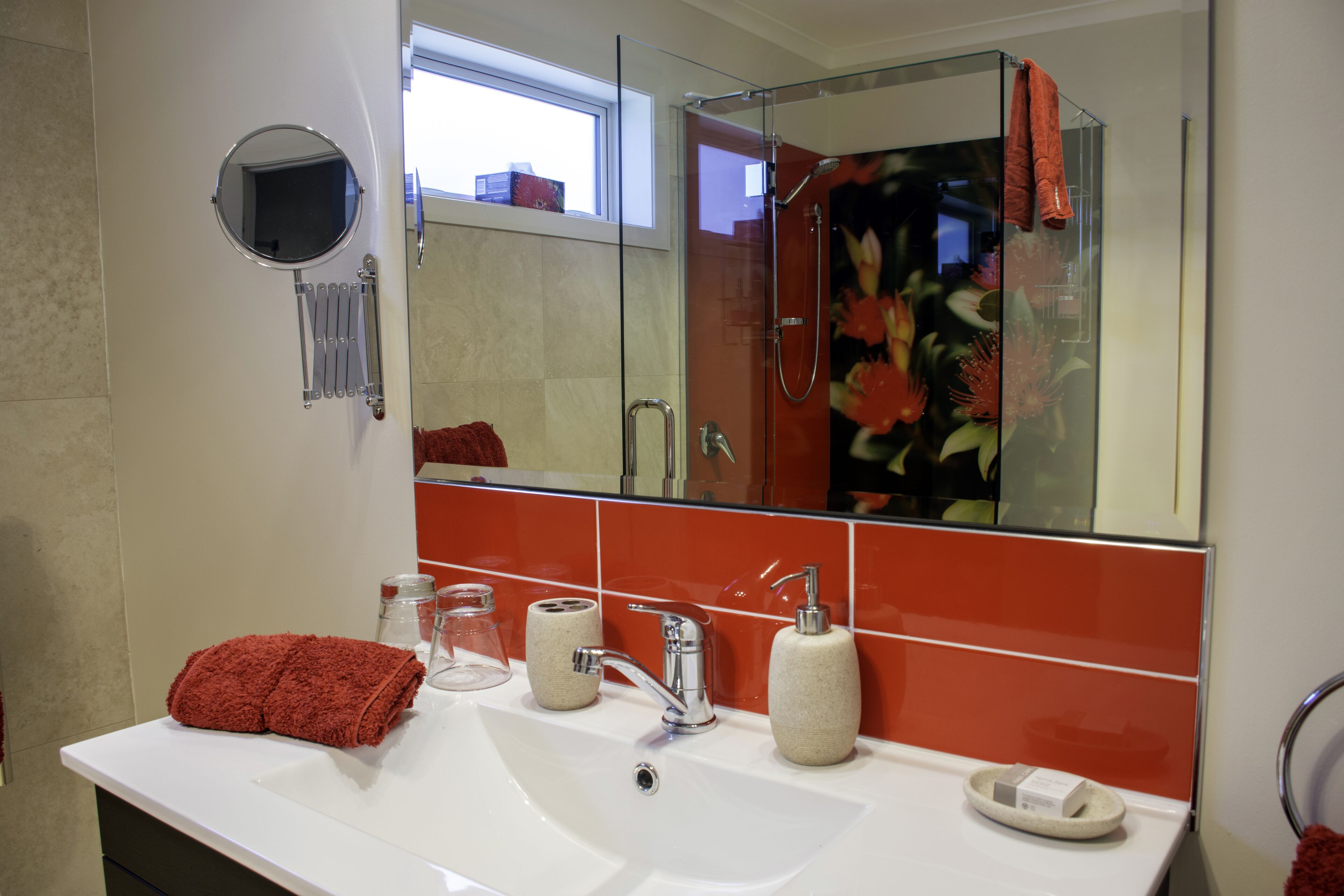 A bathroom with a white sink, a mirror, a shower, and a red towel.