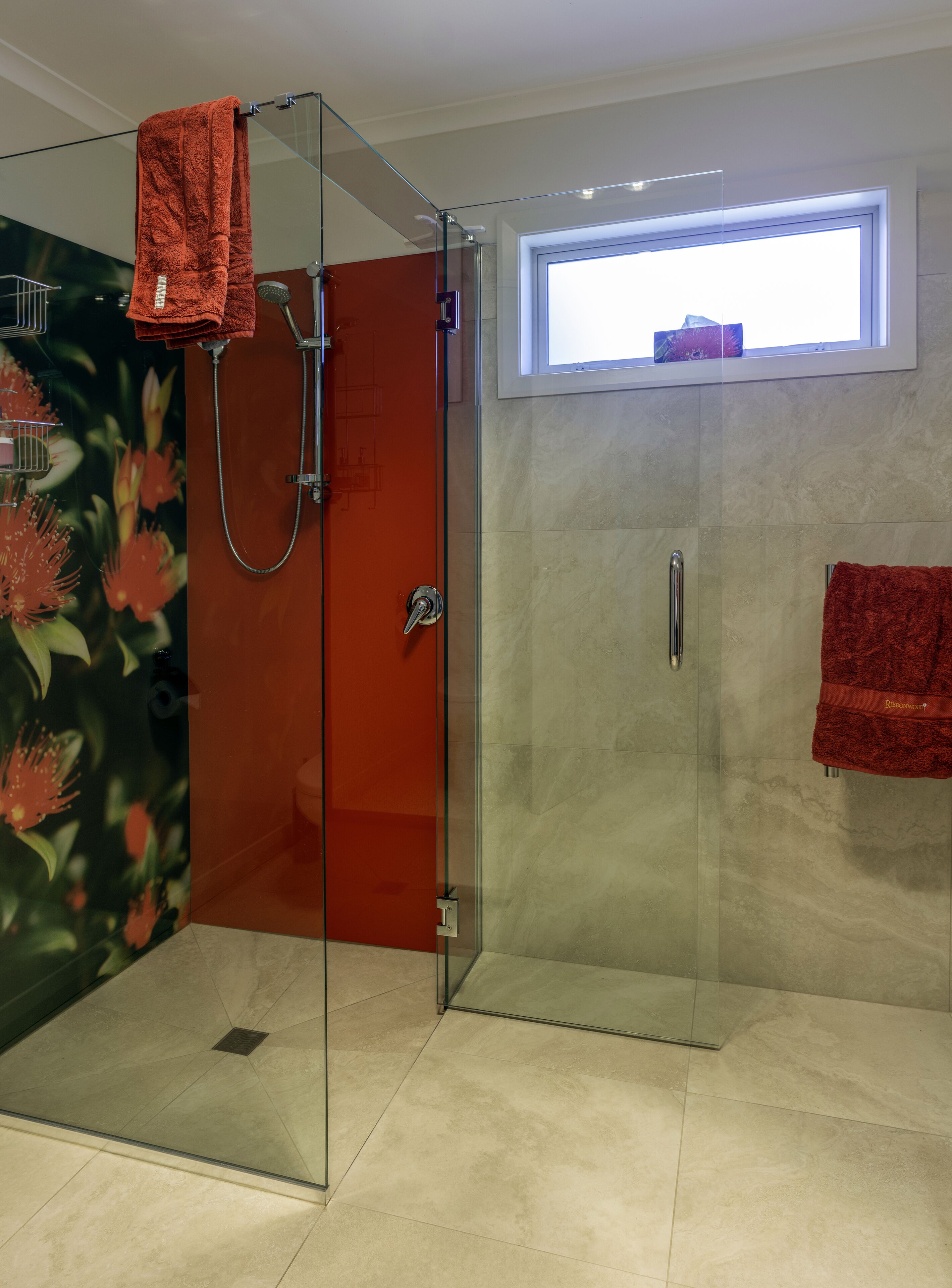 Ein modernes Badezimmer mit Duschkabine aus Glas, einem roten Handtuch und einem Fenster für natürliches Licht.