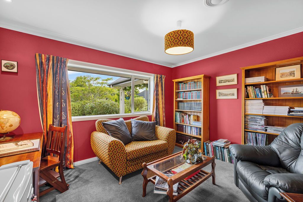 A living room with a red wall, a patterned sofa, a leather armchair, a bookshelf, and a globe on a desk.
