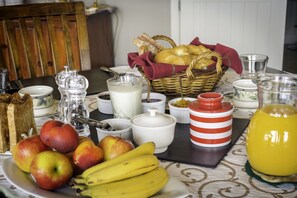 Una mesa de desayuno con pan, manzanas, plátanos, leche y una jarra de jugo de naranja.