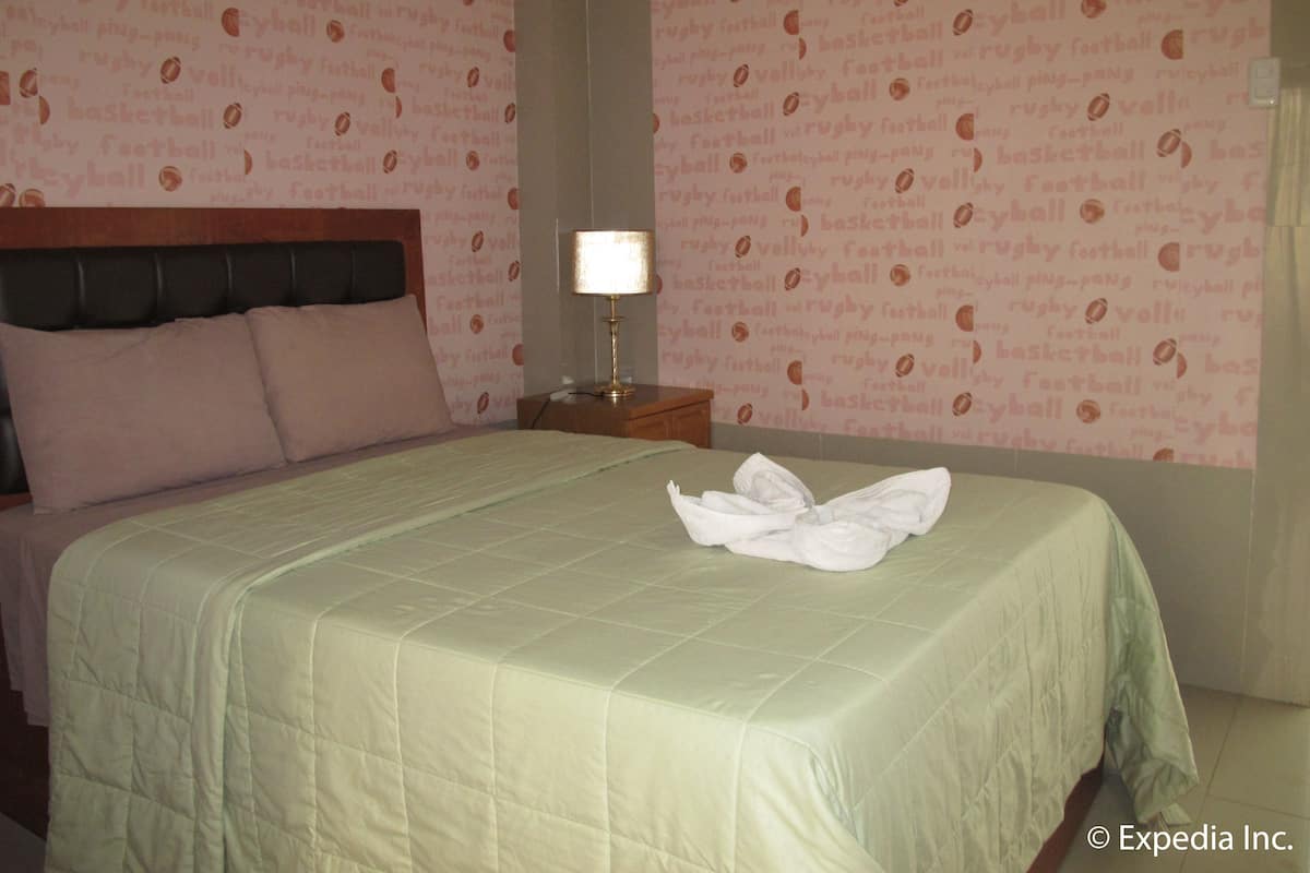 A hotel room with a bed, a nightstand, a lamp, and a wall with sports-themed wallpaper.