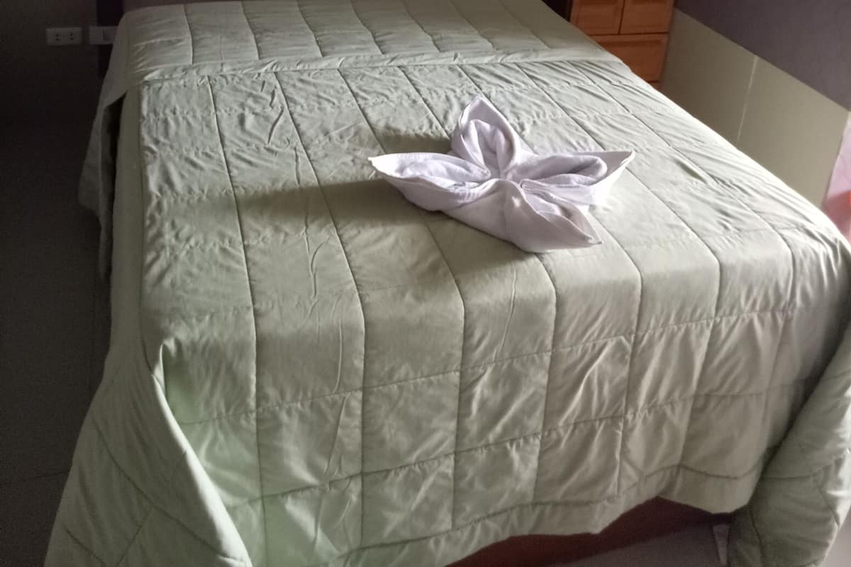 A neatly made bed with a quilt and a towel on top, a bedside lamp, and a framed picture on the wall.