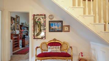 A room with a red upholstered bench, a mirror with floral decorations, and a staircase with white balusters.