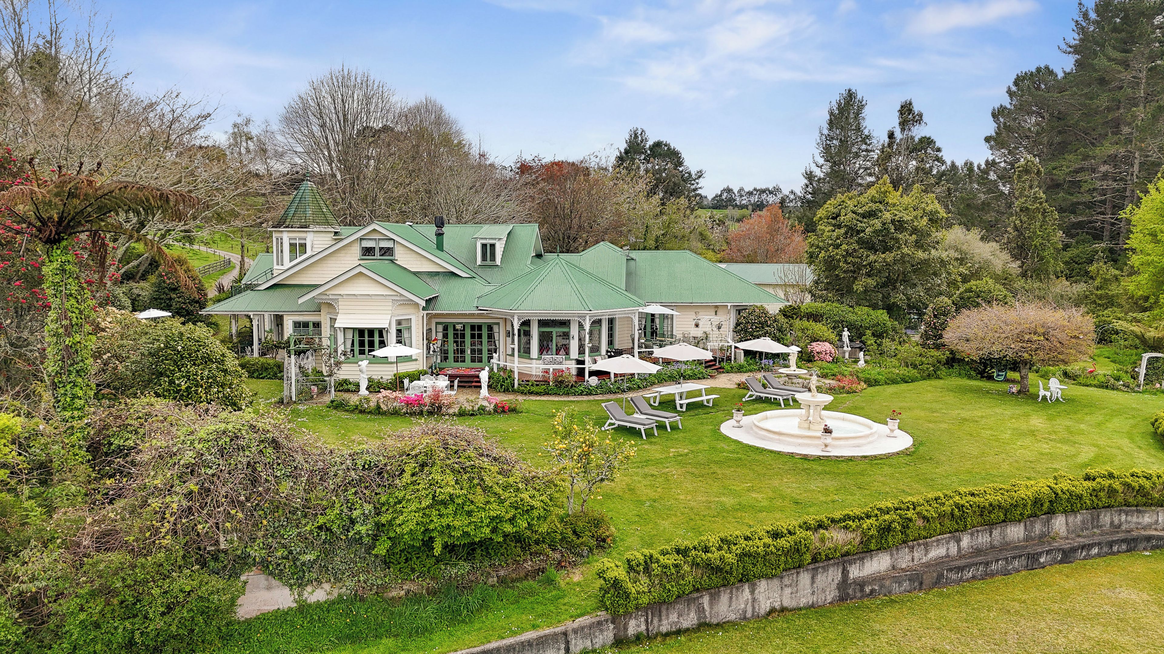 Une grande maison avec un toit végétalisé, un patio couvert et une fontaine circulaire.
