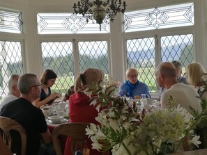 A dining area with large windows, a chandelier, and a table set for a meal. - Country Villa Estate (Hamurana)
