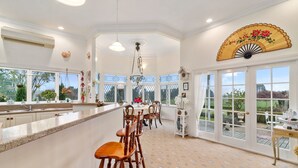 A spacious kitchen with a long counter, wooden chairs, and a large window overlooking a garden. - Country Villa Estate (Hamurana)