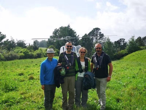 Cuatro personas de pie en un campo cubierto de hierba, con un helicóptero al fondo.