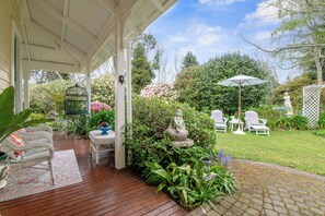 A covered patio with wicker furniture, a birdcage, and a statue of a woman. - Country Villa Estate (Hamurana)