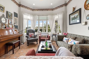 A well-furnished living room with a piano, a sofa, a chair, and a table with decorative items. - Country Villa Estate (Hamurana)