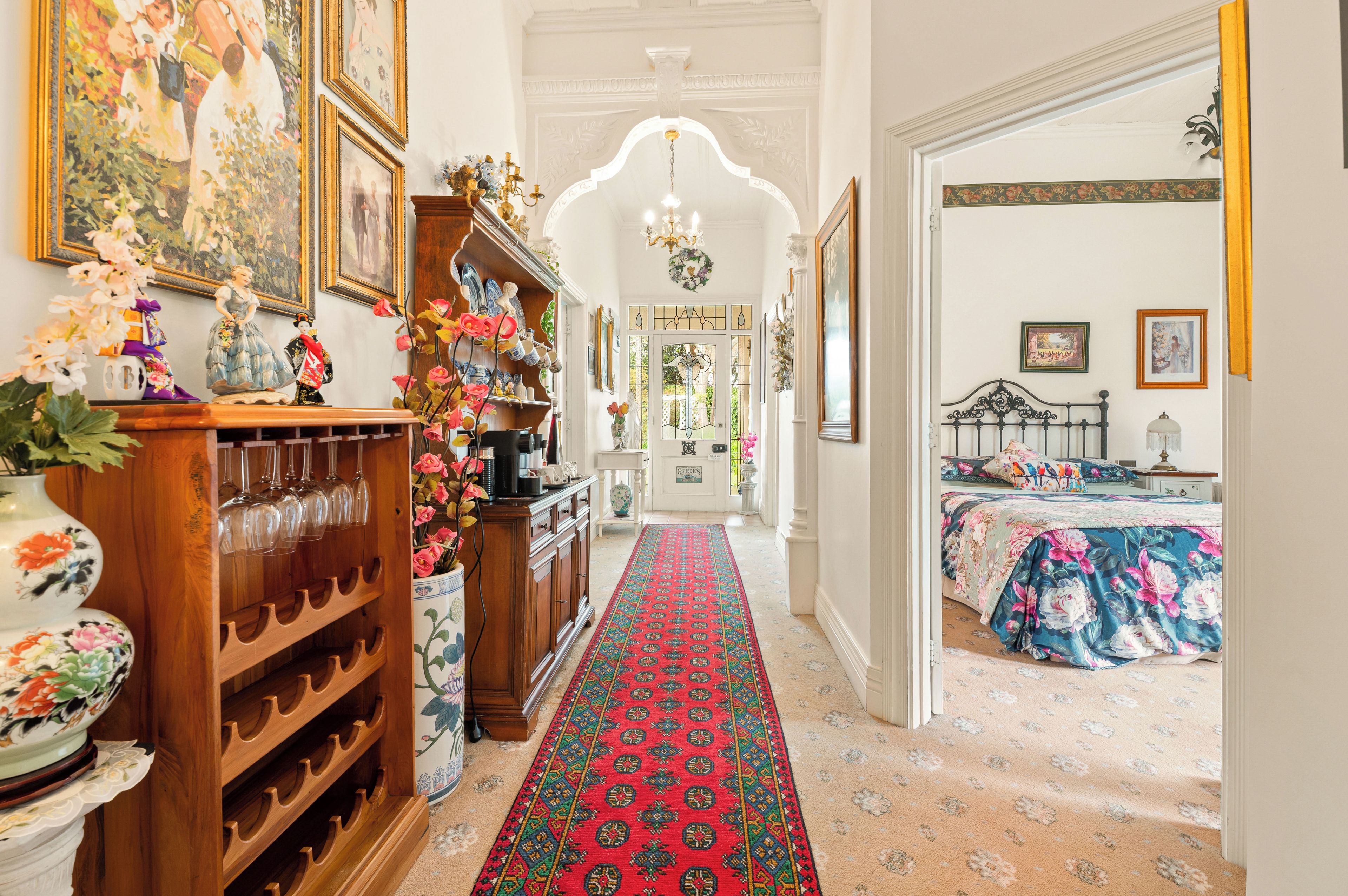 Un couloir avec un tapis rouge à motifs, des meubles en bois et divers objets décoratifs.