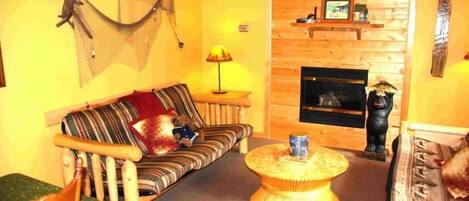 A cozy living room with a wooden sofa, a round coffee table, a fireplace, and a bear statue.