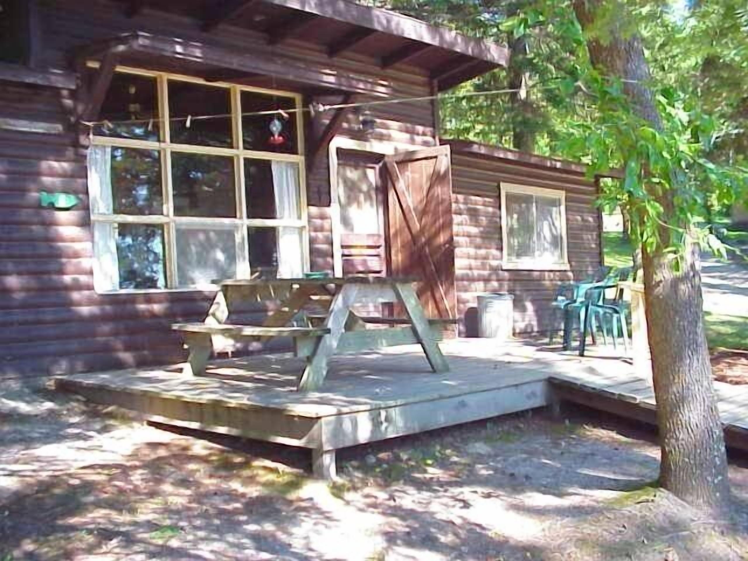 Eine rustikale Holzhütte mit einer Holzterrasse, einem überdachten Außenbereich zum Sitzen und einem großen Fenster.