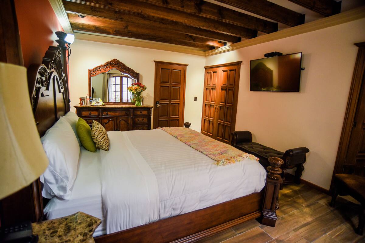 A bedroom with a wooden bed, a dresser, a mirror, and a television on the wall.