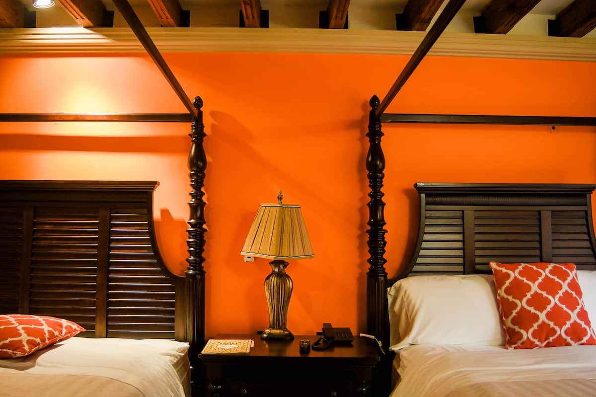A room with a four-poster bed, a bedside table with a lamp, and two pillows.