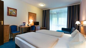 A hotel room with two beds, a desk with a computer, a chair, a TV, and a large window with curtains. - Hotel St. Georg Gmbh (Bad Aibling)