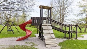 Un parque infantil con un tobogán rojo, estructuras de madera para escalar y columpios.