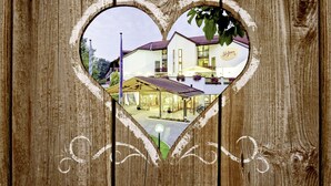 Una ventana en forma de corazón con vista a un edificio que incluye una zona exterior cubierta y un cartel con el nombre "St. Michael".