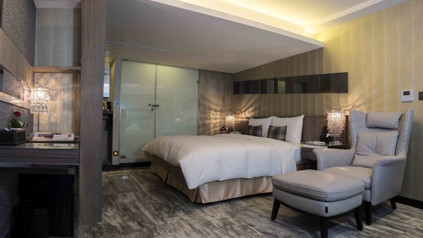 A modern hotel room with a bed, a sitting area with a chair, a desk with a lamp, and a large mirror. - Hotel I Journey (Taipei)