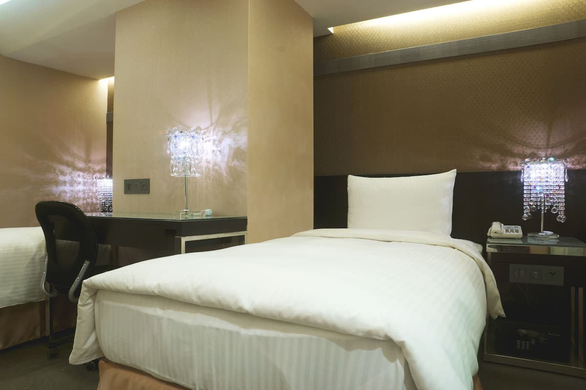 A hotel room with a bed, a desk, a chair, and a phone on a bedside table.