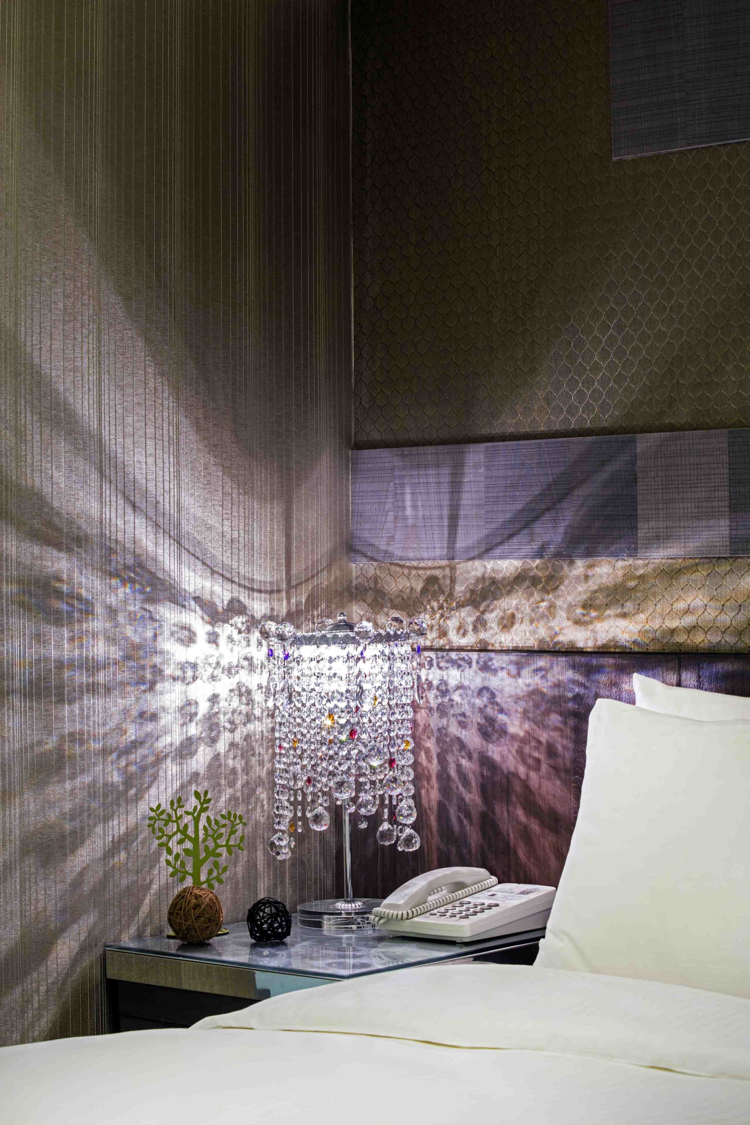A hotel room with a bed, a bedside table with a telephone, and a decorative hanging light fixture.