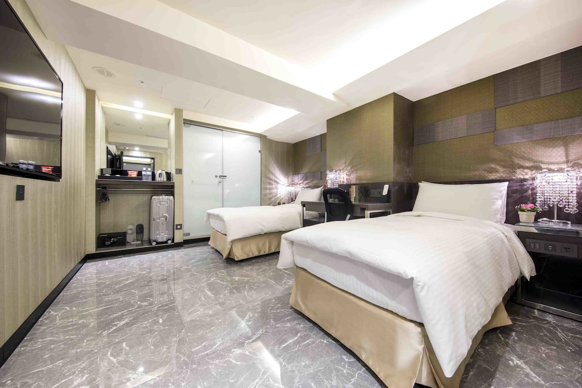 A hotel room with two beds, a desk, a chair, a wardrobe, and a bathroom.