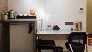 A compact hotel room with a kitchenette, a small desk with a chair, a potted plant, a water bottle, a bag of chips, a coffee maker, a decorative lamp, and a thermostat on the wall. - Hotel I Journey (Taipei)