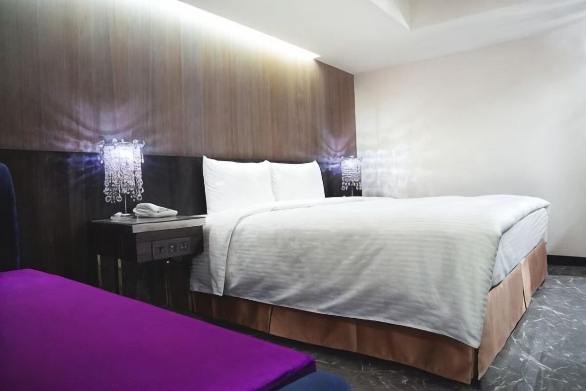 A hotel room with a bed, a nightstand, a purple chair, and a marble floor.