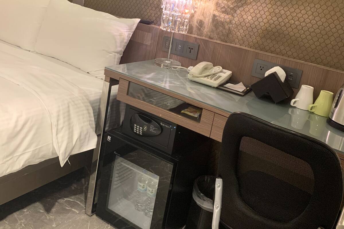 A hotel room with a bed, a desk with a phone, a coffee maker, a trash bin, and a minibar.