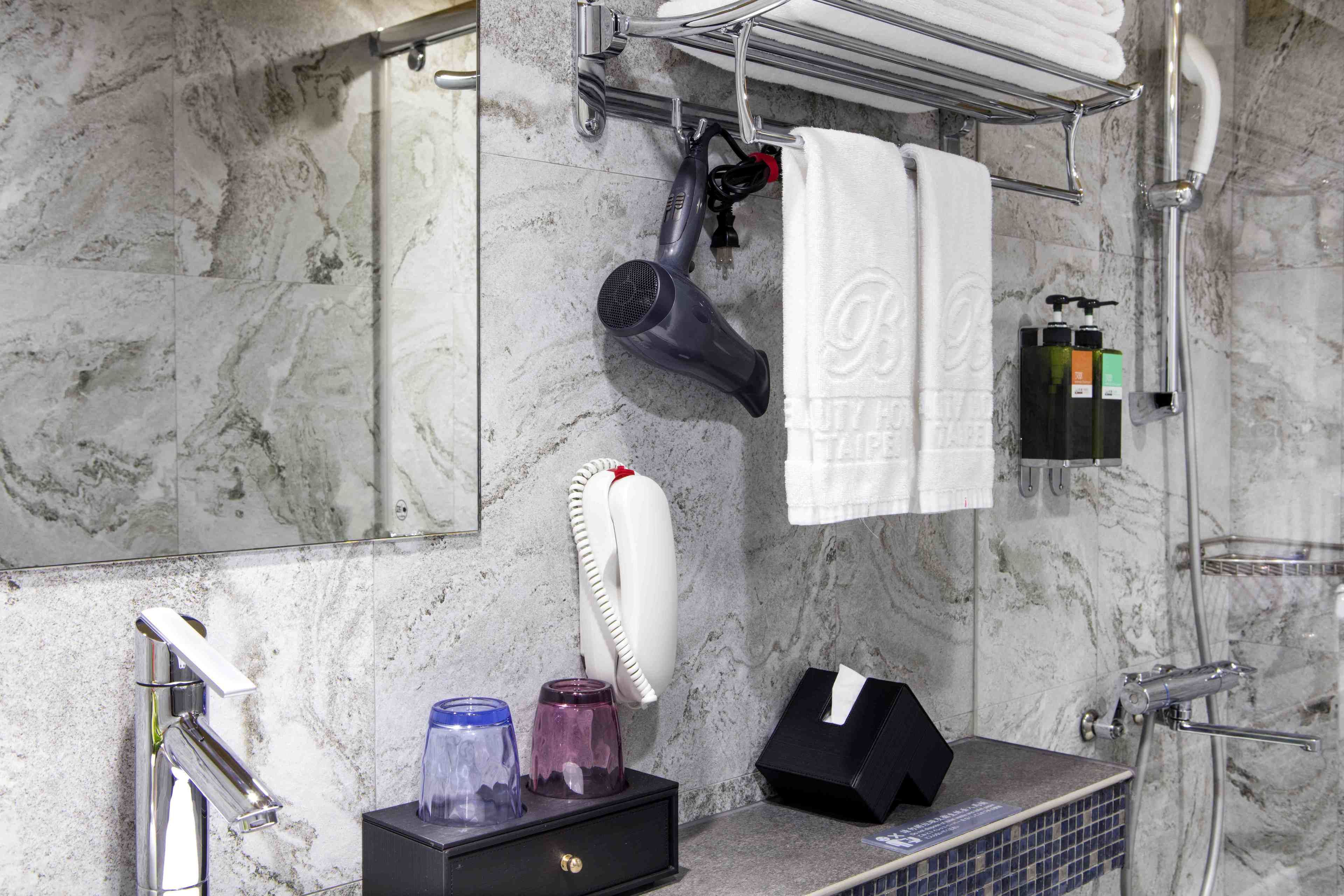 A bathroom with a marble wall, a hairdryer, a towel rack, a mirror, and a sink with toiletries.