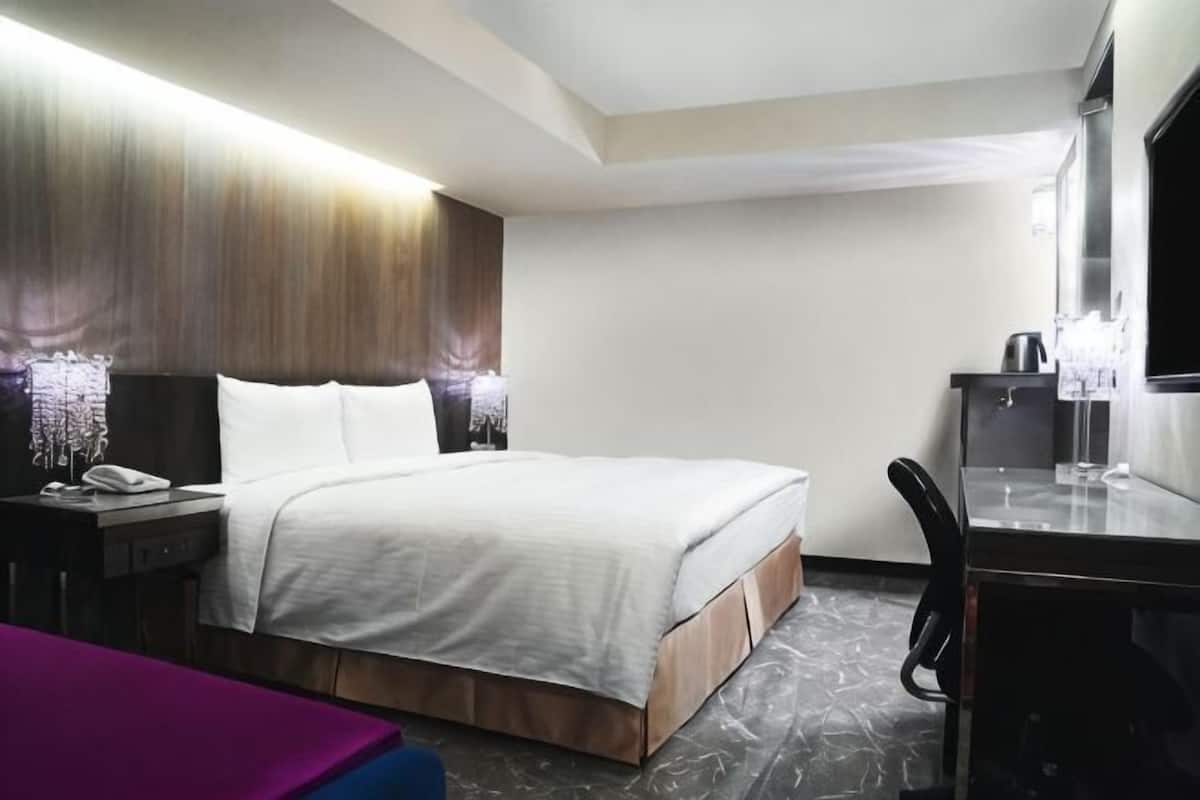 A hotel room with a bed, bedside table, lamp, and a desk with a chair.