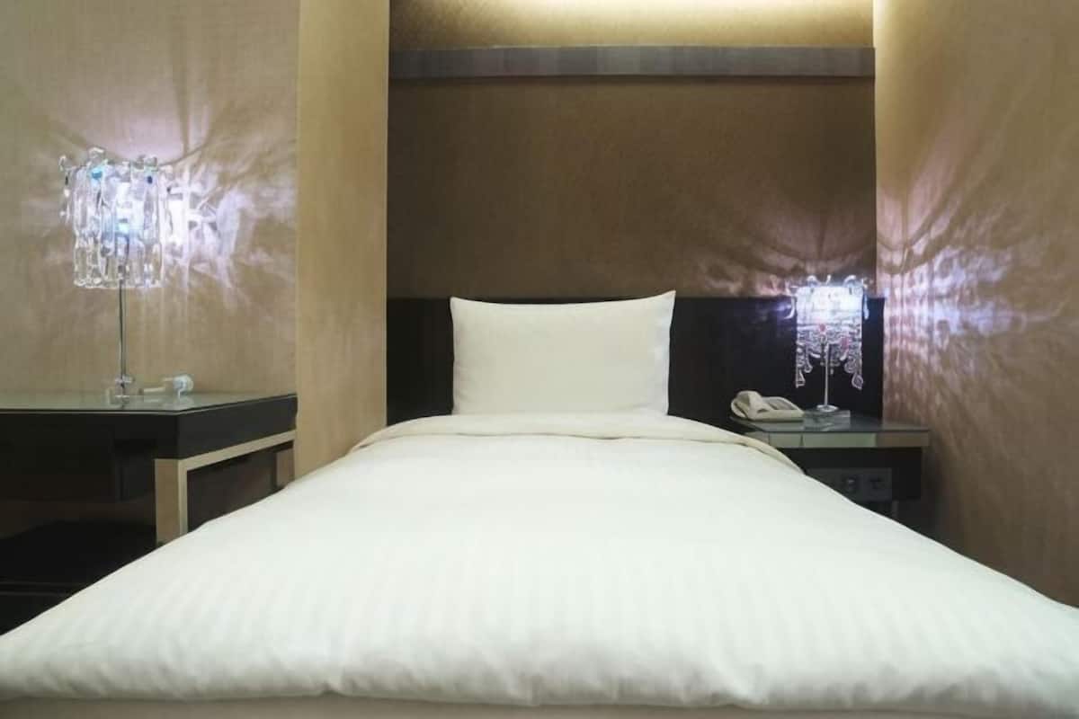 A hotel room with a bed, bedside tables, a lamp, and a phone.