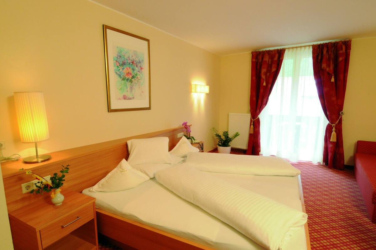 A hotel room with a large bed, a bedside table with a lamp, a potted plant, and a painting on the wall.