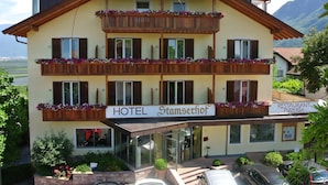 A two-story hotel with balconies adorned with flowers, a restaurant, and a sign indicating it is a hotel and pizzeria. - Hotel Stamserhof (Andriano)