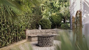 A stone fire pit in a garden with a stone bench, surrounded by lush greenery and a stone wall. - Hotel Stamserhof (Andriano)