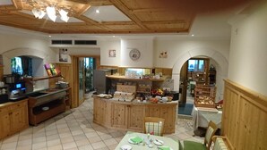 A rustic kitchen with wooden cabinets, a central island, and a dining area with a table set for two. - Hotel Stamserhof (Andriano)