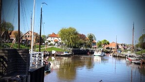 A calm river with boats docked, a bridge, and houses along the riverbank. - Up Diek (Wittmund)