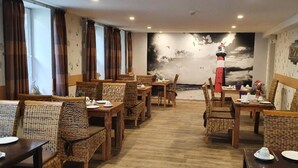 A restaurant with wicker furniture, a mural of a lighthouse, and a wooden floor. - Up Diek (Wittmund)