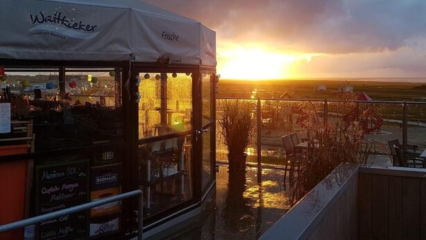 A restaurant with a view of the sunset, outdoor seating, and a tent with signage. - Up Diek (Wittmund)
