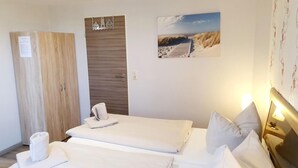 A hotel room with two beds, a wooden wardrobe, a door with a small window, and a beach-themed wall decoration. - Up Diek (Wittmund)
