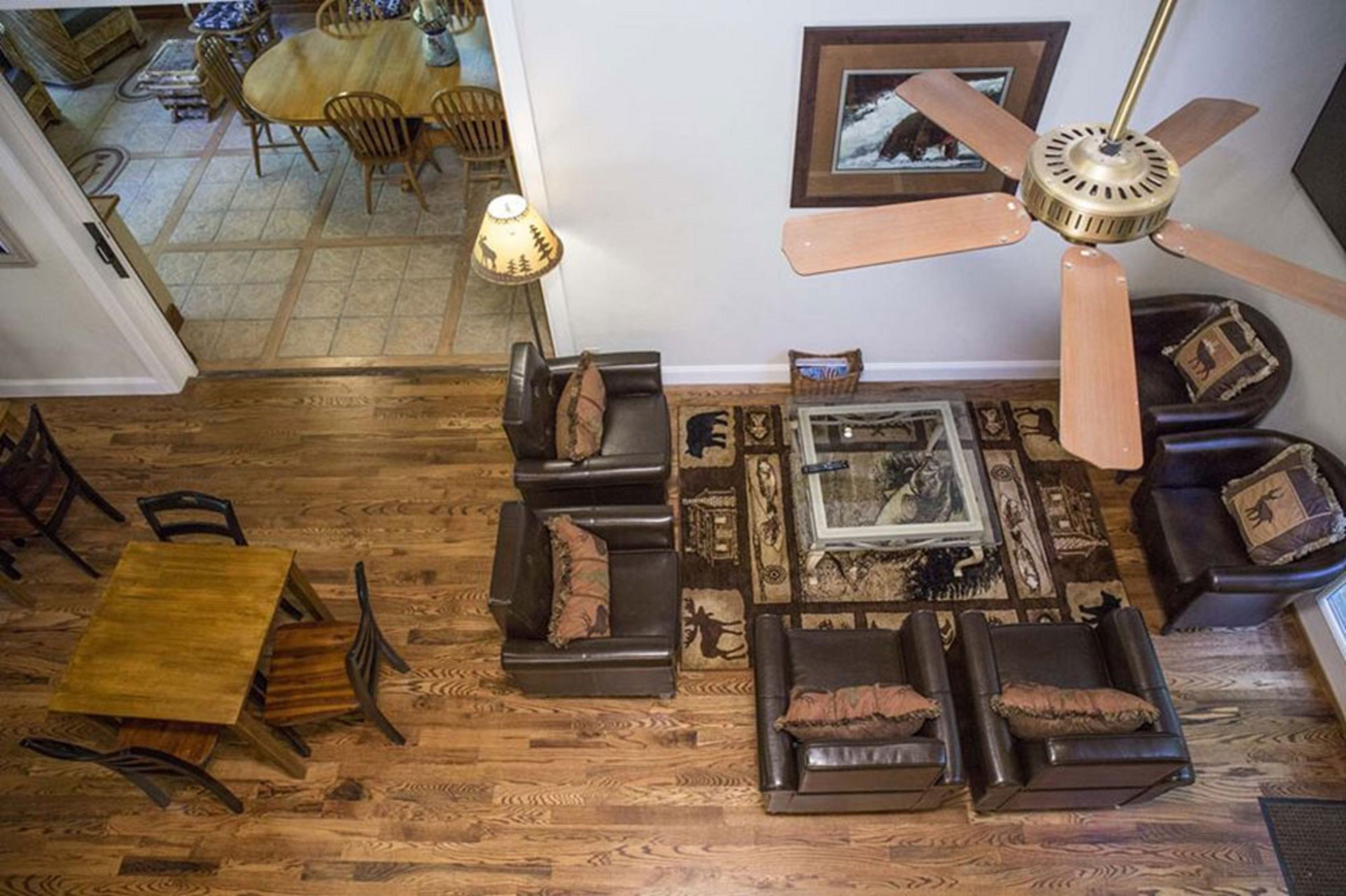 Un salon doté d’un plancher en bois, d’un ventilateur de plafond, d’une cheminée et d’un coin repas avec une table et des chaises en bois.