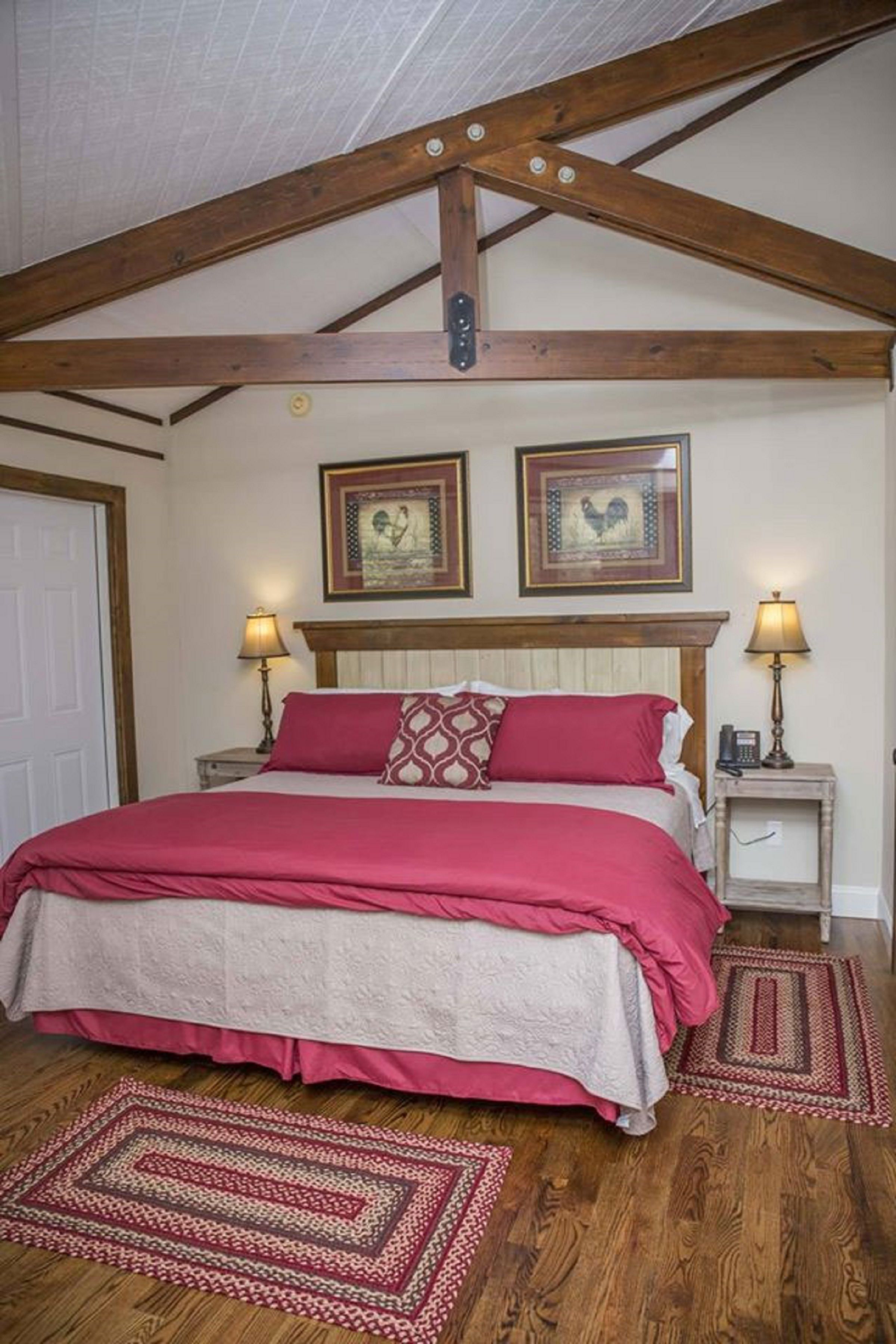 Un dormitorio con techo de madera, una cama con ropa de cama roja, dos lámparas de noche y dos cuadros en la pared.