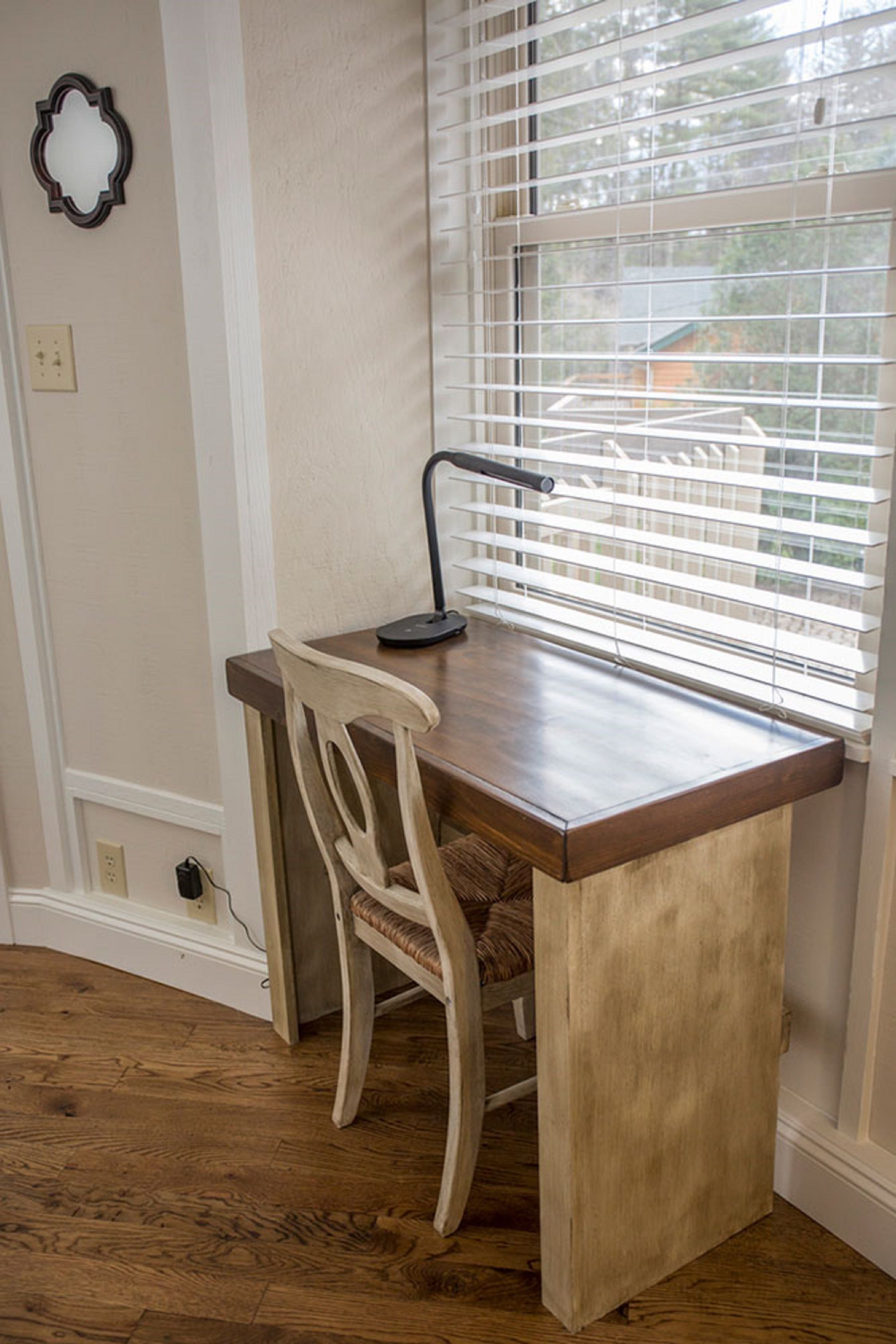 Un bureau d’angle avec une chaise, une lampe et une fenêtre équipée de stores.