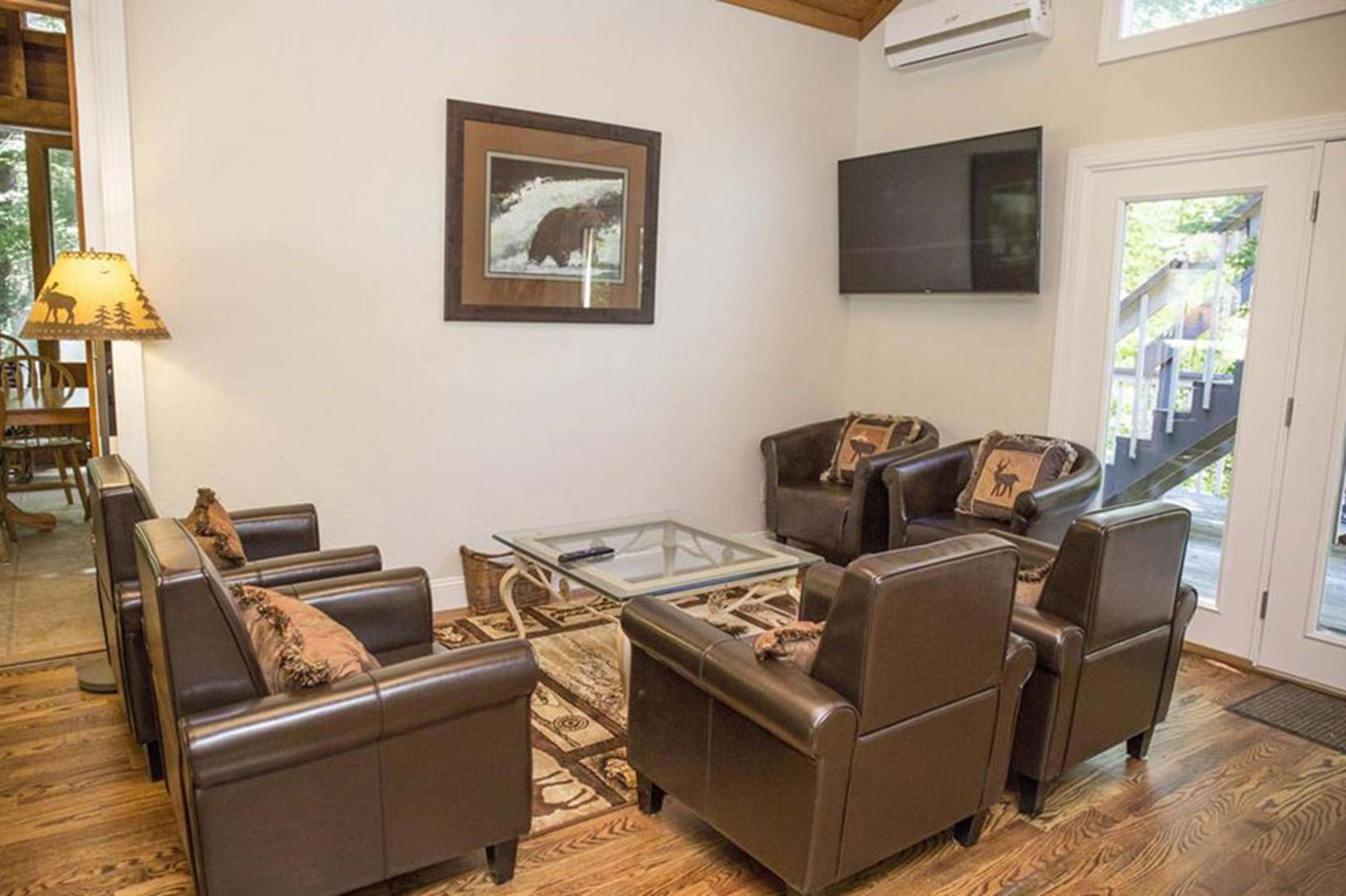 A living room with leather sofas, a glass coffee table, and a framed picture of a bear.