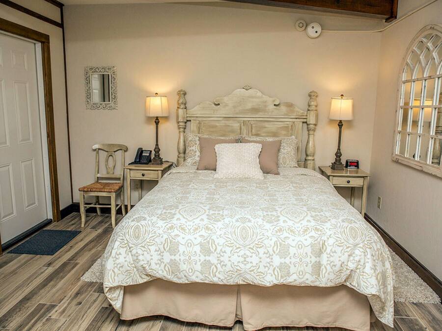 A neatly arranged bedroom with a large bed, two bedside tables with lamps, a chair, and a mirror on the wall.