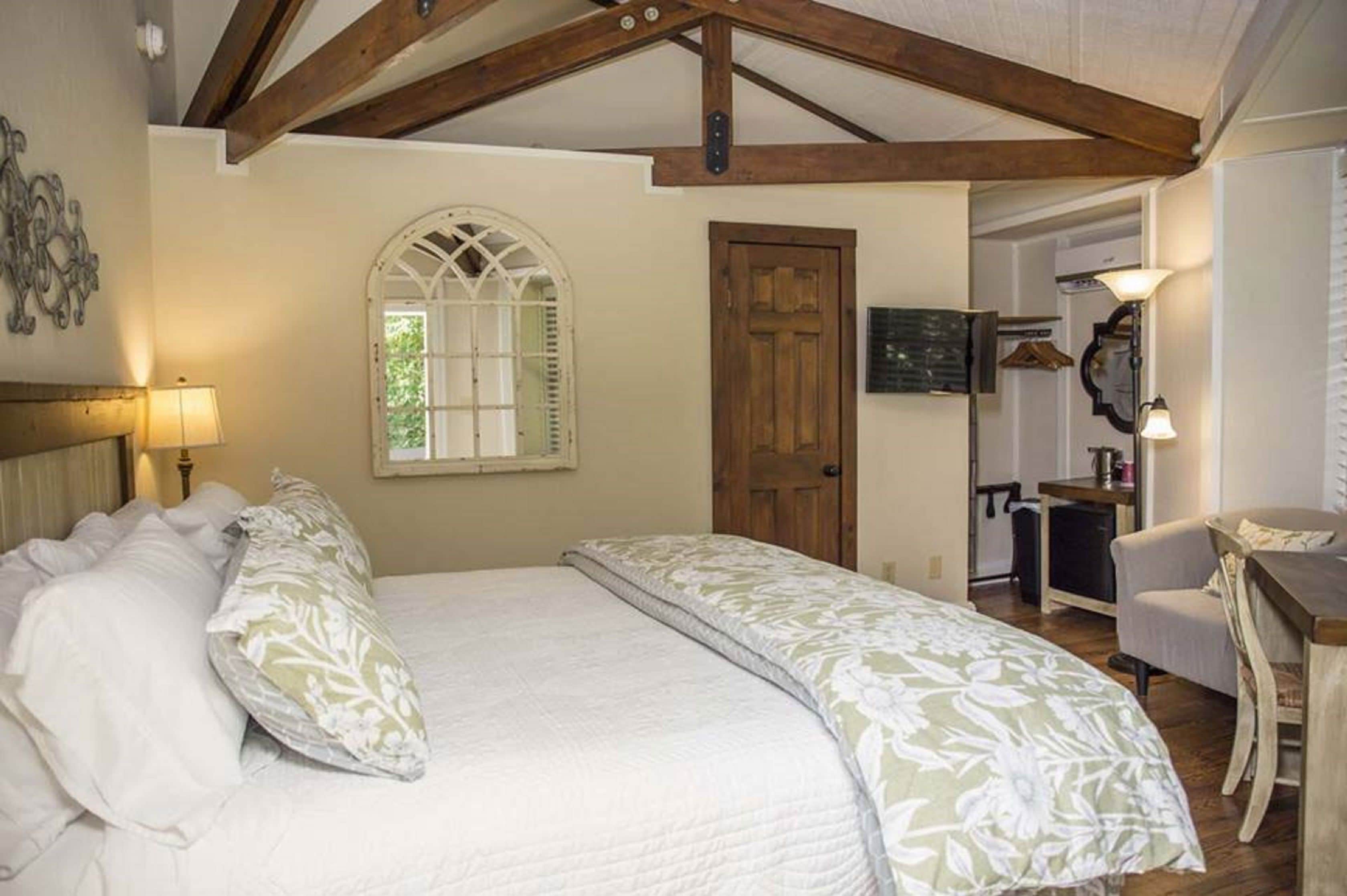 A bedroom with a large bed, a wooden door, a desk, and a chair.