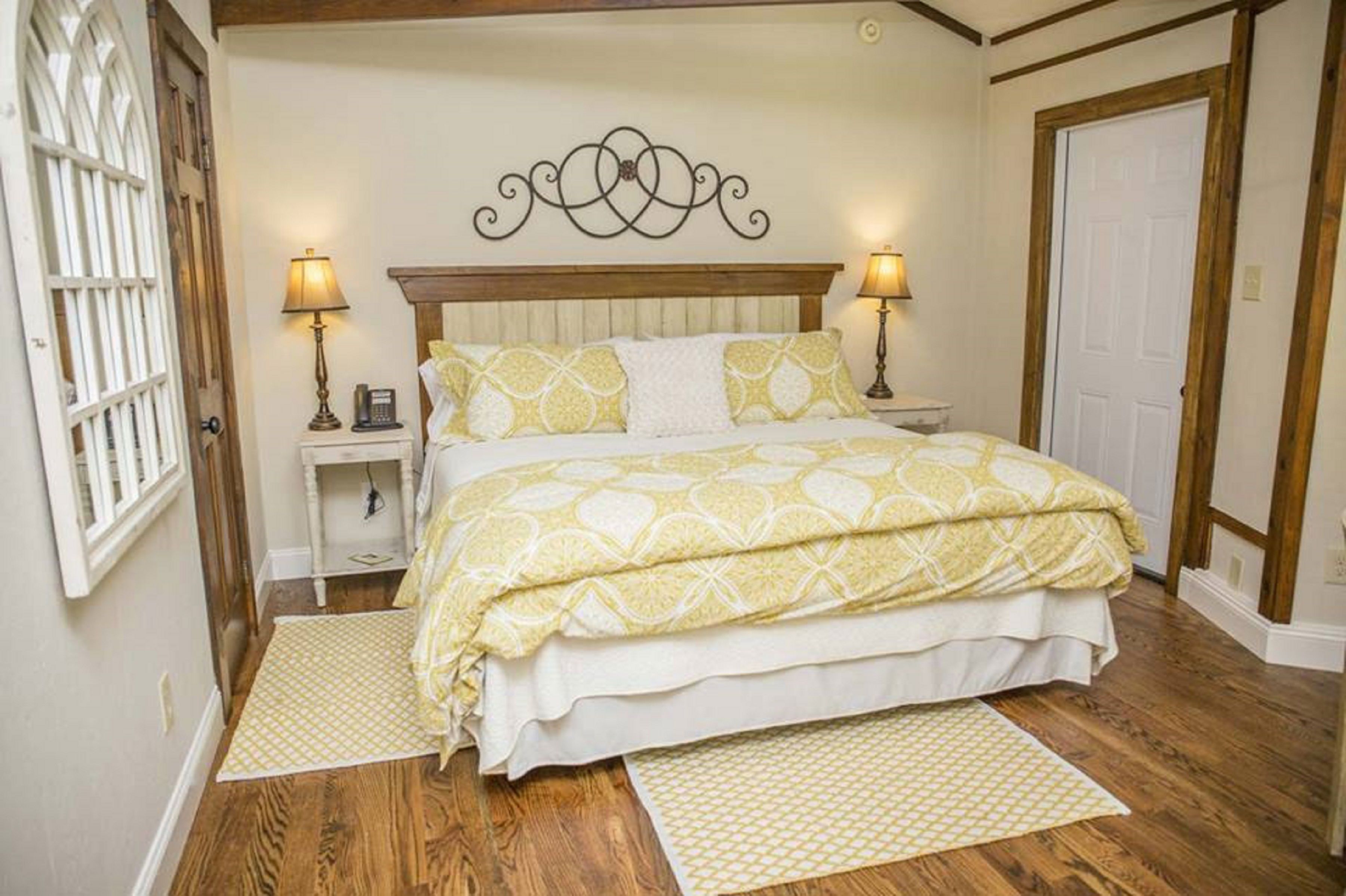 A bedroom with a wooden headboard, two bedside lamps, a patterned bedspread, and a wooden floor.
