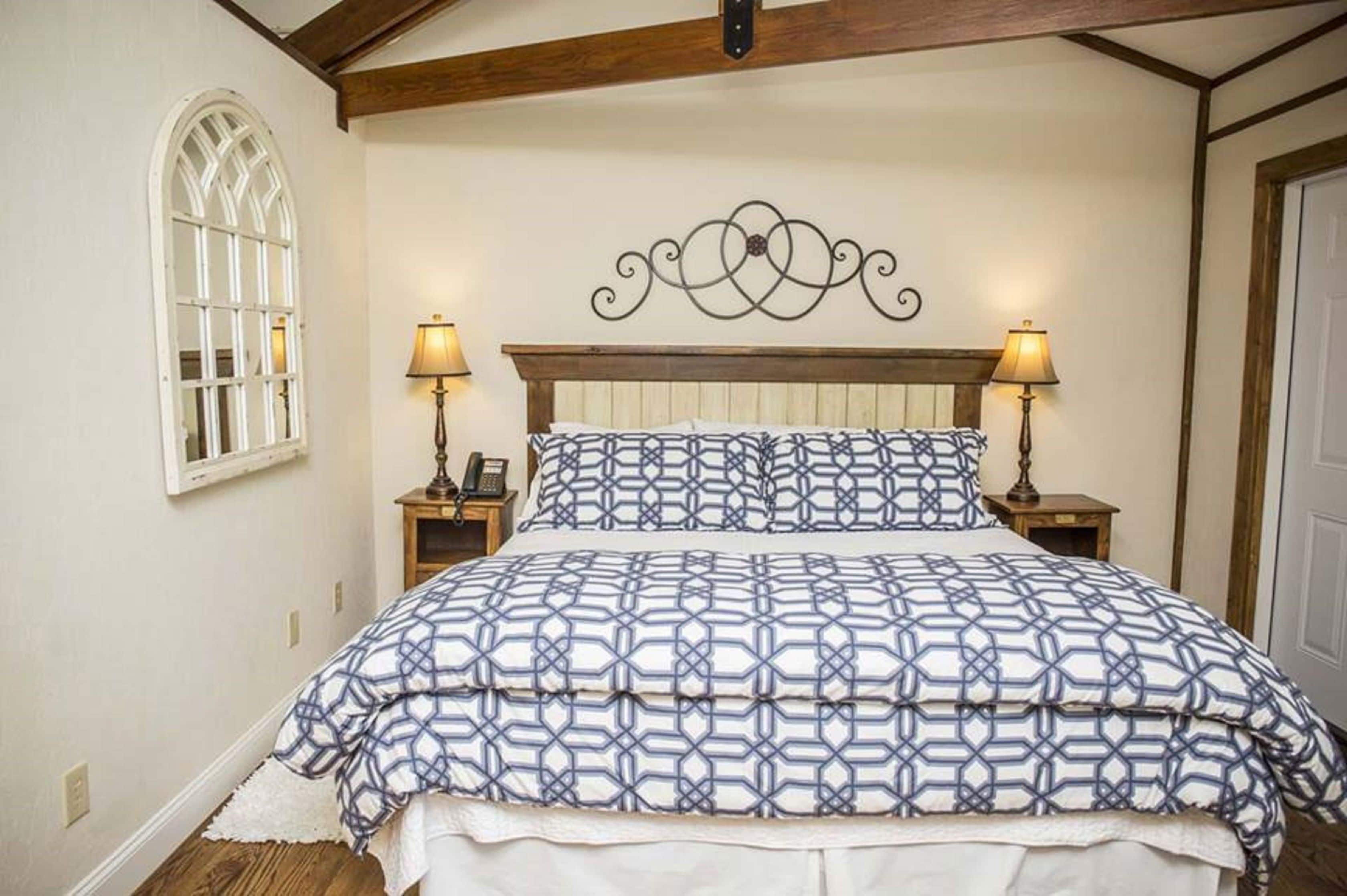 A bedroom with a large bed, two bedside tables, a decorative wall piece, and a window with a white frame.