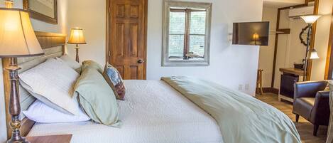 A bedroom with a large bed, two bedside lamps, a wooden door, a window, a TV, and a chair.